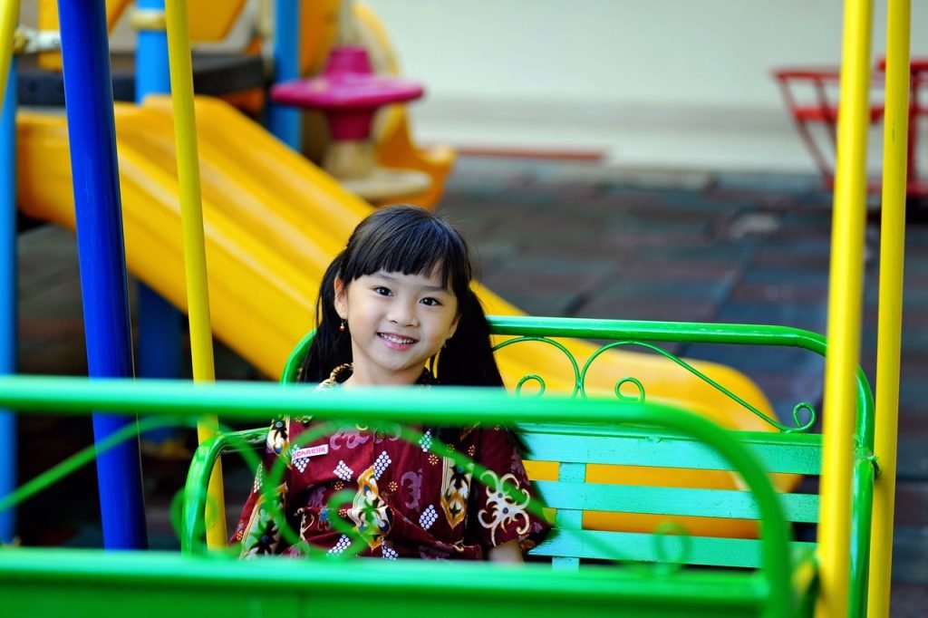 Happy young girl smiling on a green swing at a vibrant playground.